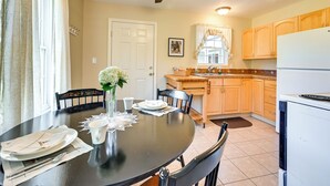 A dining area with a round table set for four, a ceiling fan, and a kitchen in the background. - Quiet Killingworth Rental w/ Deck & Grill! (Killingworth)