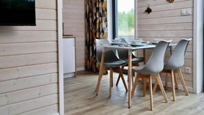 Un comedor moderno con una mesa y sillas de madera, un televisor montado en la pared y un ventanal con vistas a zonas verdes.
