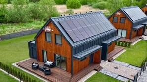Una casa moderna con techo inclinado, ventanas amplias y una terraza con mobiliario exterior.