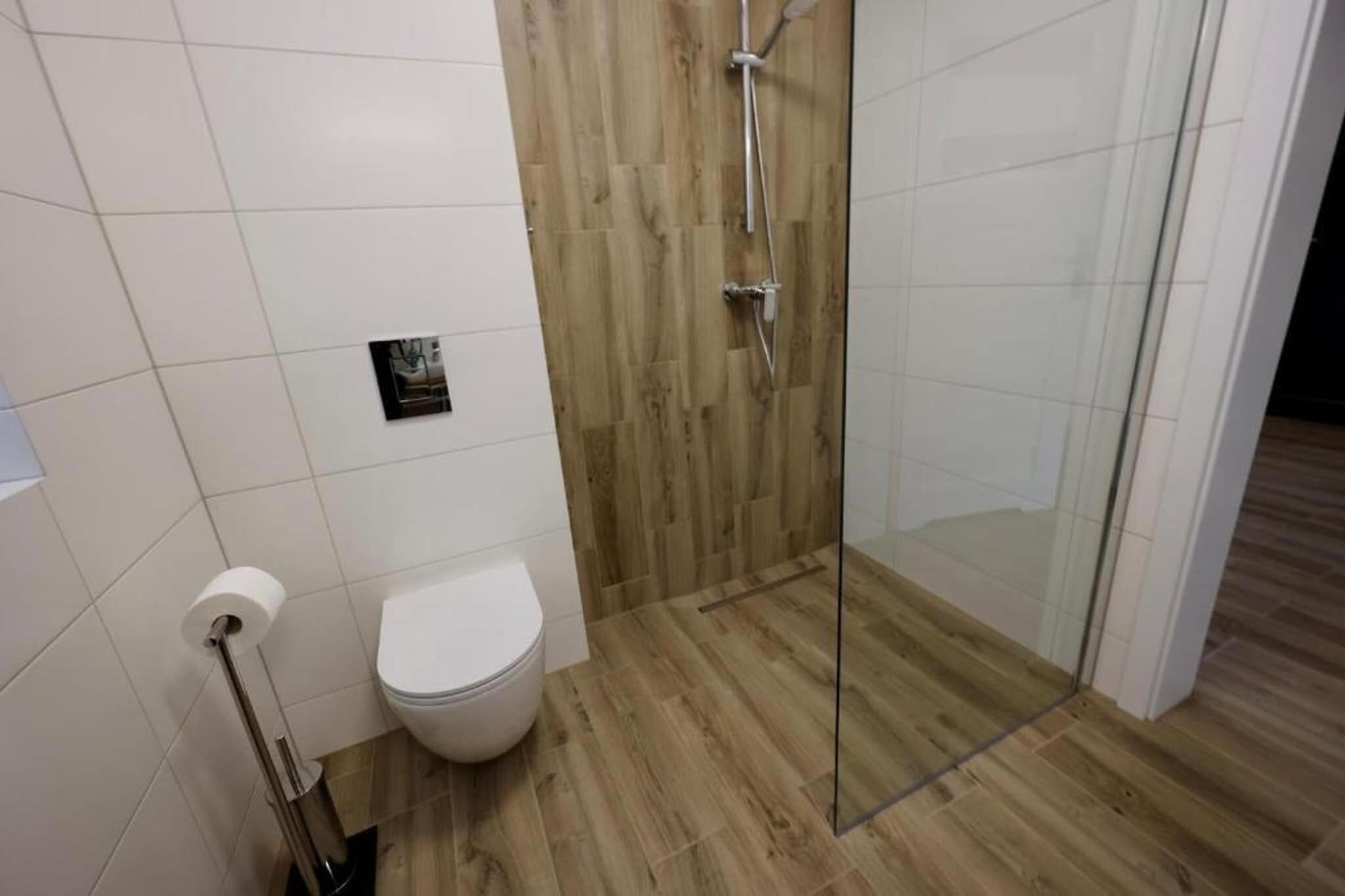 A bathroom with a toilet, a shower with a glass door, and a wooden floor.