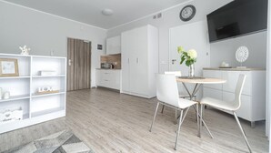 A modern, minimalist living space with a dining area, kitchen, and a large TV mounted on the wall.