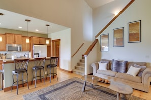 A spacious living area with a kitchen, bar stools, a sofa, and a staircase.