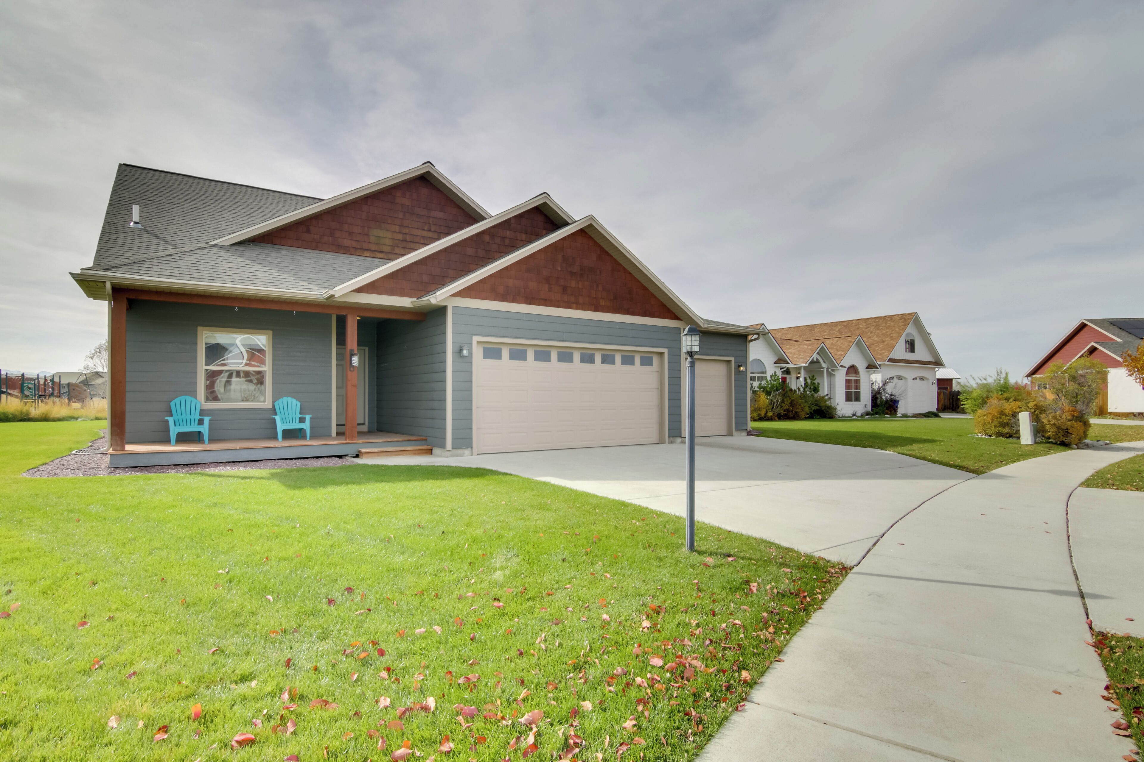 A single-story house with a garage, a front porch with two chairs, and a well-maintained lawn.