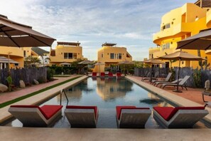 Un área de piscina con tumbonas y sombrillas, rodeada de edificios amarillos.