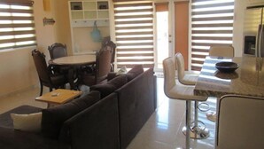Une cuisine moderne avec un coin bar, une table à manger avec des chaises et un espace salon comprenant un canapé et une table basse.
