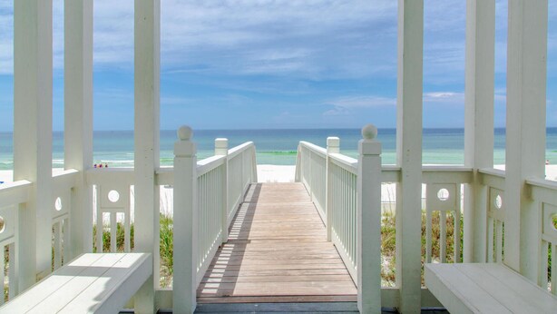 A wooden pier leading to a beach with white railings and a clear view of the ocean.