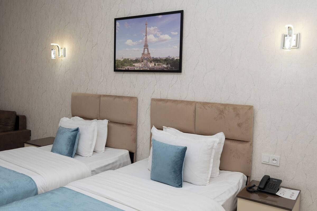 Une chambre d’hôtel avec deux lits, une table de chevet avec un téléphone et une image de la Tour Eiffel accrochée au mur.
