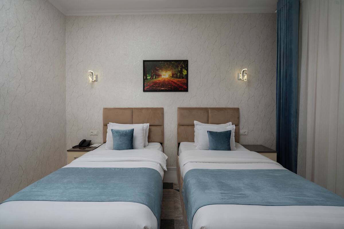 Une chambre d’hôtel avec deux lits, une table de chevet, un tableau et une fenêtre avec des rideaux.