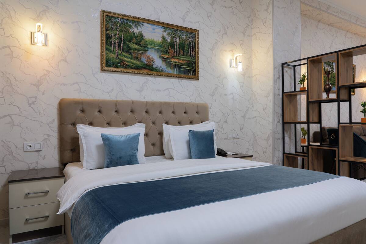 Une chambre à coucher avec un grand lit, une table de chevet, un tableau accroché au mur et une étagère en bois ornée de plantes.