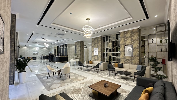 En moderne hotellobby med reception, siddeområde og et stort bogreol.
