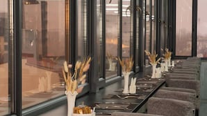 A row of tables with chairs, each table has a vase with dried plants and a napkin holder.