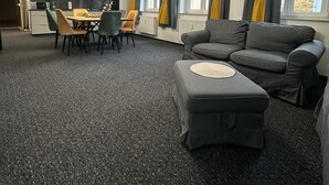 Moderni olohuone, jossa on harmaa sohva, ruokapöytä tuoleineen ja taustalla keittiötila.