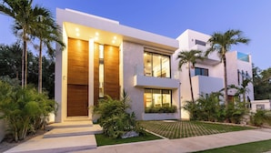 A modern two-story house with a large wooden door, a balcony, and a well-maintained lawn.