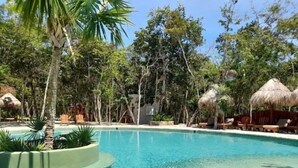 A clear pool surrounded by palm trees and thatched-roof structures.