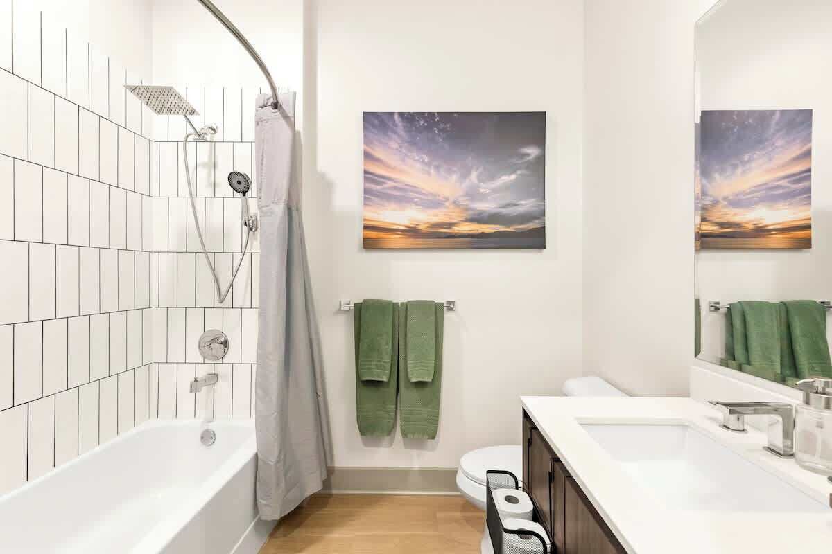 Un baño moderno con bañera, ducha, inodoro y lavabo. Dos toallas verdes cuelgan de la pared.