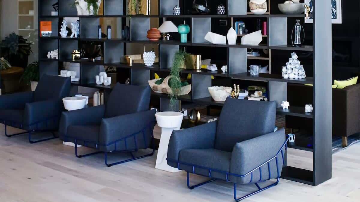 A modern interior with three dark blue armchairs, a white side table, and a black shelving unit filled with various decorative items.