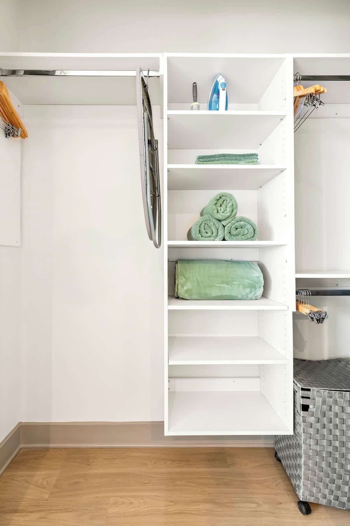 Un placard blanc avec des étagères pour ranger les vêtements pliés, une tringle pour suspendre les vêtements et un bac de rangement.