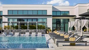 Ein modernes Hotel mit Schwimmbad, Liegestühlen und einer überdachten Sitzgruppe.