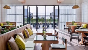 Ein modernes Interieur mit Sitzbereichen, Tischen und großen Fenstern mit Blick auf die grüne Umgebung.
