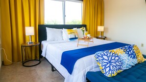 A hotel room with a bed, two bedside tables, a window with curtains, and a view of greenery outside. - King Studio - One
 (Georgetown)