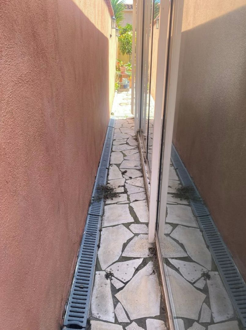A narrow outdoor corridor with a tiled floor and a drainage grate.
