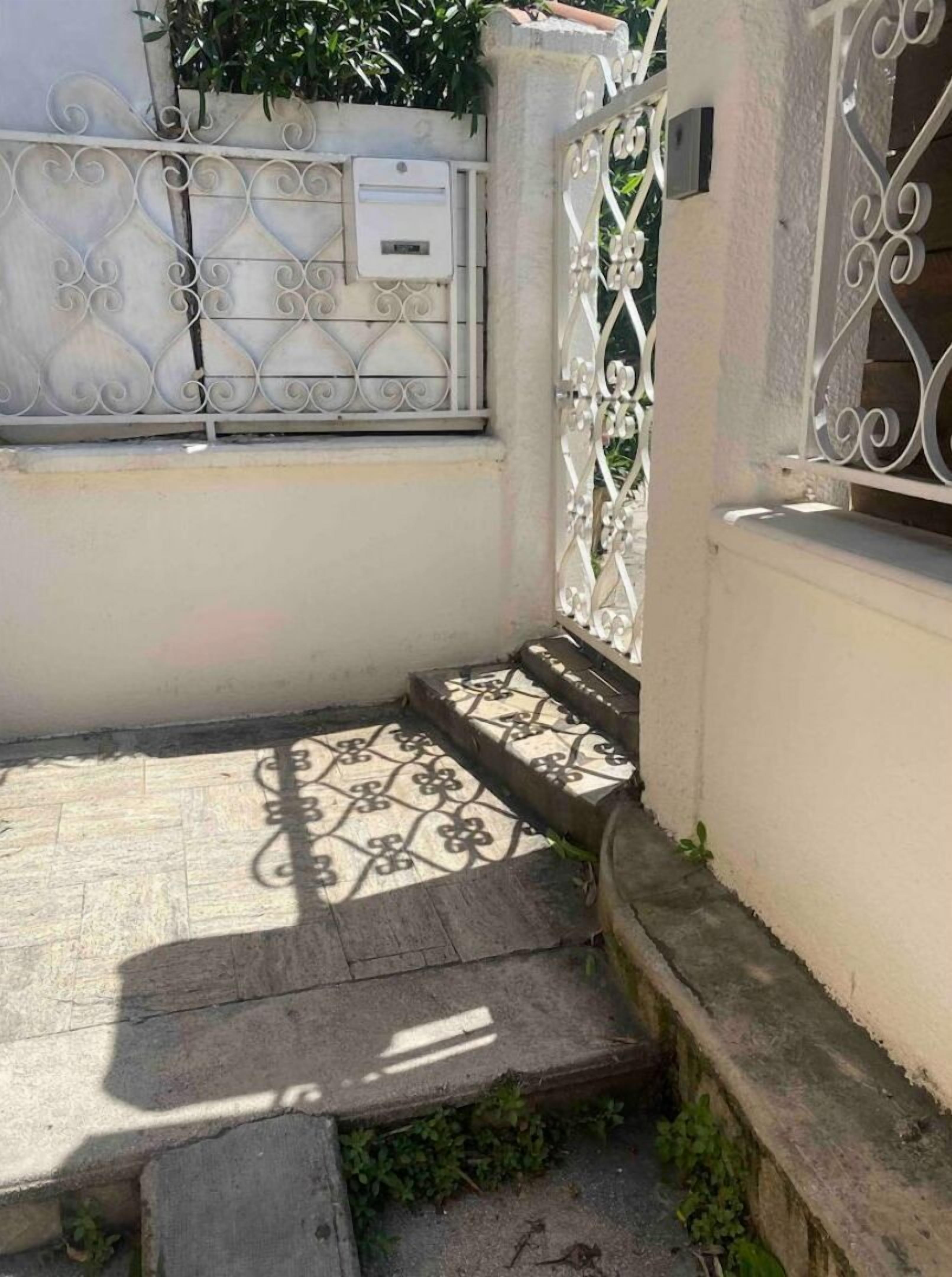 Un petit espace extérieur doté d’un sol carrelé, d’un portail en métal et d’un mur avec une boîte aux lettres.