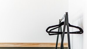 Ein Zimmer mit Holzboden, einem schwarzen Metall-Kleiderständer, einem kleinen Holztisch mit Lampe und einer dunkelgrünen Wand.