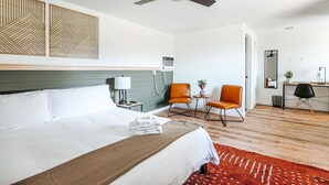 A hotel room with a bed, a desk, two chairs, a ceiling fan, and a wall-mounted air conditioner. - Grey Pine Lodge | King Deluxe | BEST Location & Amenities! (Waynesboro)