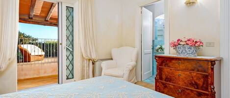 A bedroom with a bed, a chair, a dresser, and a view of a balcony.