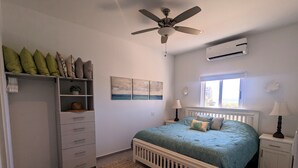A bedroom with a bed, a wardrobe, a ceiling fan, an air conditioner, and a window with a view.