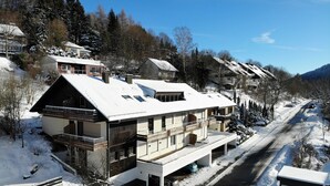 Ein mehrstöckiges Wohngebäude mit verschneitem Dach, einem Balkon und einer Einfahrt mit geparkten Autos.
