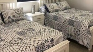 A bedroom with two beds, a nightstand, and a window with a blind.
