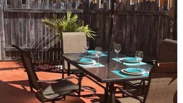An outdoor dining area with a table set for four, surrounded by chairs, under a large umbrella.