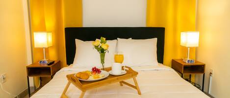 A hotel room with a bed, two bedside tables with lamps, a tray with breakfast items, and a clock on each table.