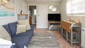 Un salon moderne avec un canapé, un téléviseur et une cuisine visible à travers une porte ouverte.