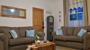 Una sala de estar acogedora con dos sofás marrones, un baúl de madera y un reloj grande en la pared.