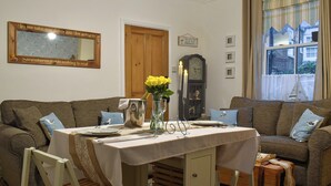 Una sala acogedora con una mesa de comedor para dos personas, un reloj y vistas a la calle desde una ventana.