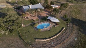 An aerial view of a residential property with a swimming pool, a covered patio, and a large house with a blue roof. - Stunning Fredericksburg Ranch House with Pool and Hot Tub! (Fredericksburg)
