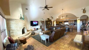 A spacious living area with a stone fireplace, leather furniture, and a television mounted on the wall. - Stunning Fredericksburg Ranch House with Pool and Hot Tub! (Fredericksburg)