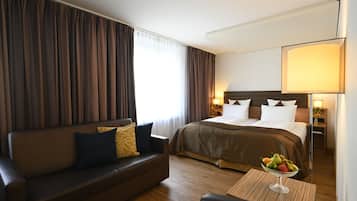 A hotel room with a bed, a sofa, a table with fruit, and curtains.