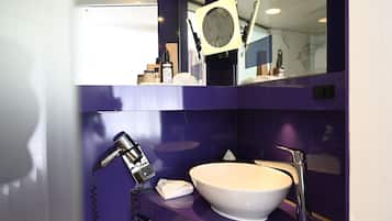 A bathroom with a white sink, a handheld showerhead, and a mirror with a round frame.