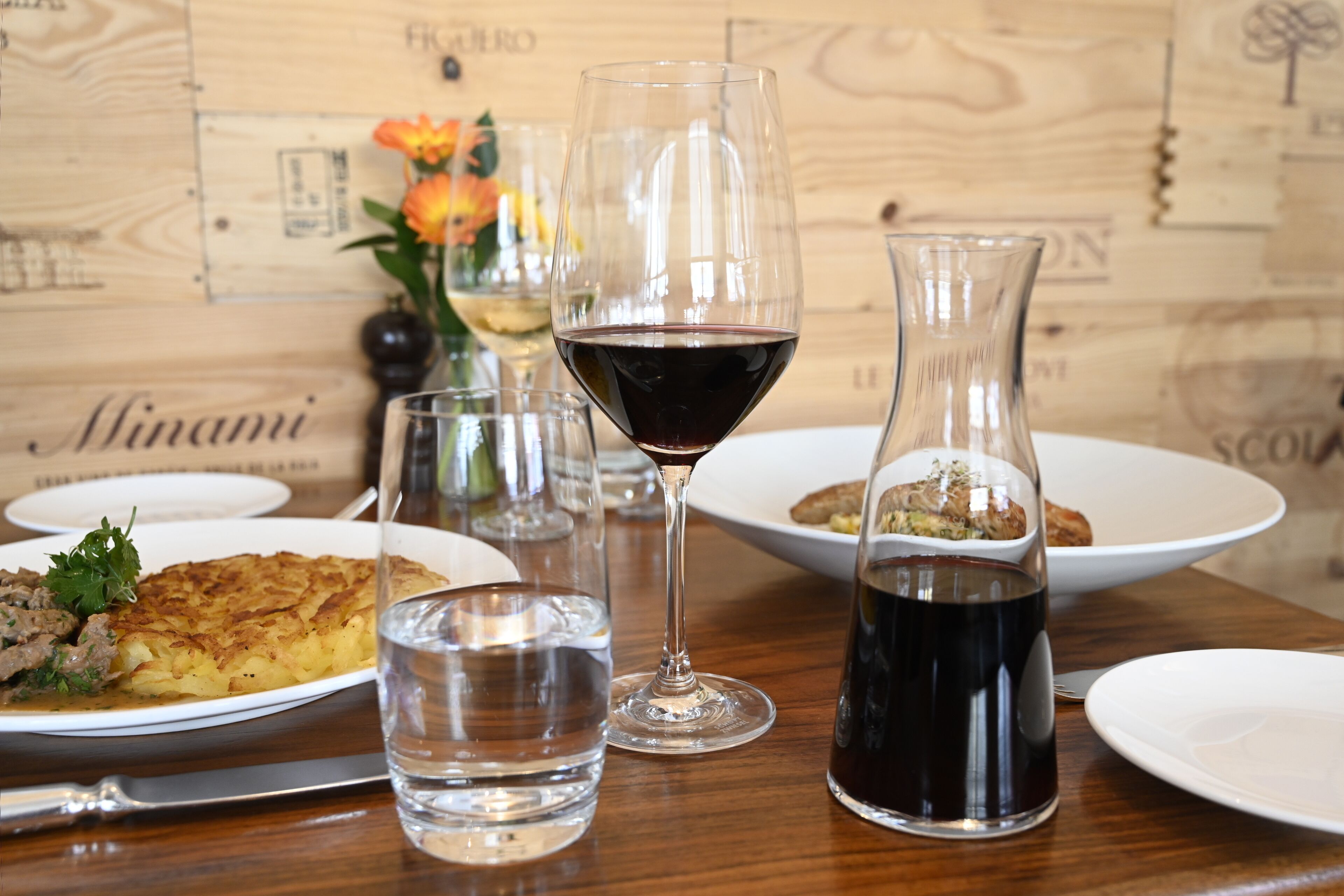 A dining table with plates of food, glasses of water and wine, and a vase with flowers.