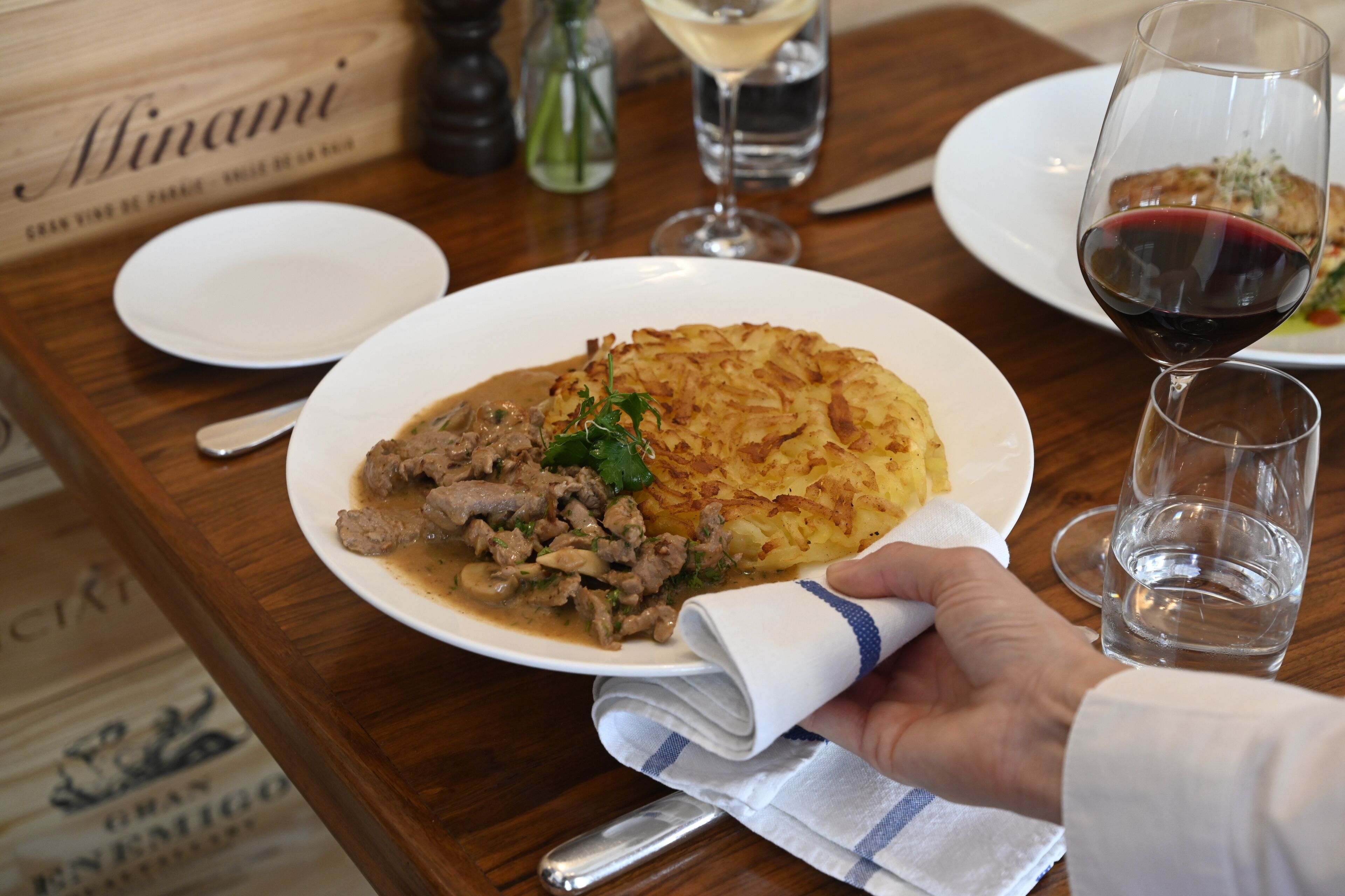 A dining table with a plate of food, a glass of red wine, and a bottle of water.