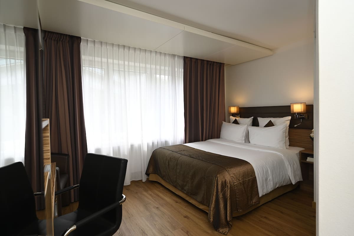 A hotel room with a large bed, a desk, and a chair.