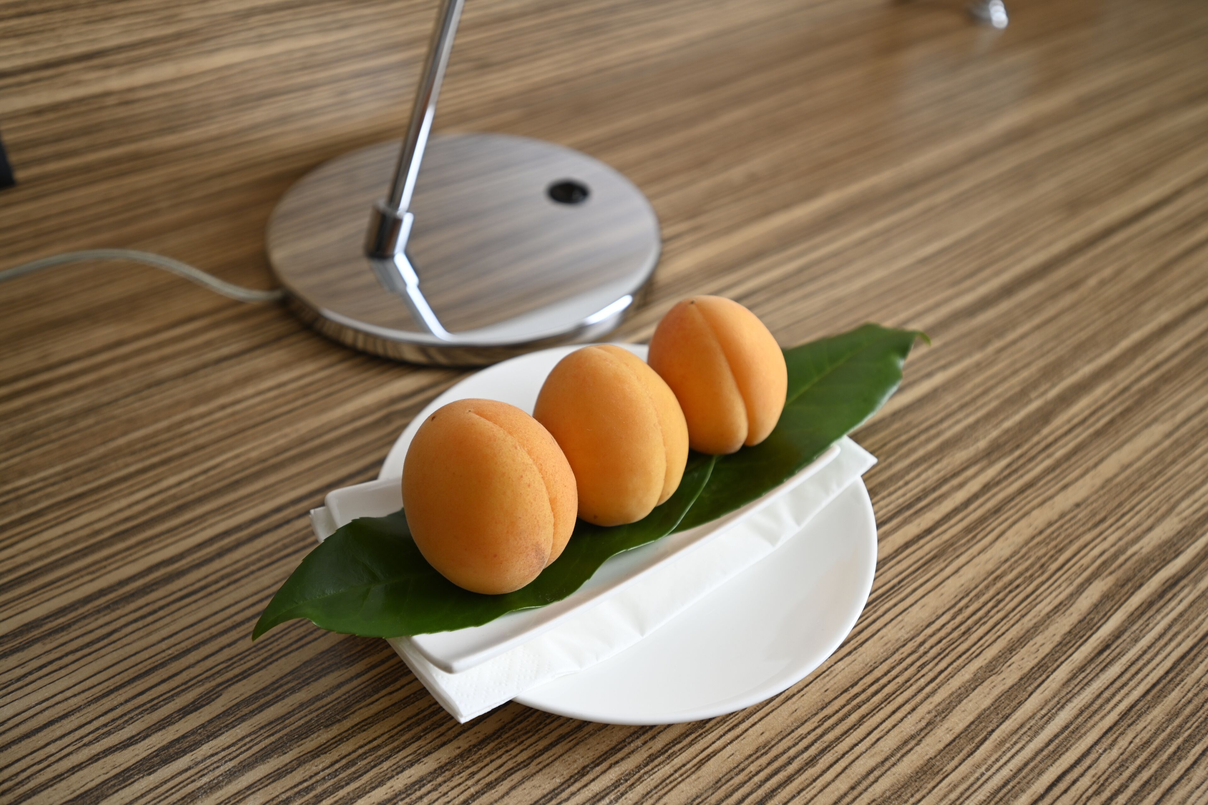 A wooden table with a white plate holding three round, orange-colored objects and a green leaf.