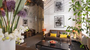A modern living room with a brown sofa, a coffee table with fruit, and a lamp. There are framed pictures on the walls and a plant in the corner. - Hotel Stoller (Zürich)
