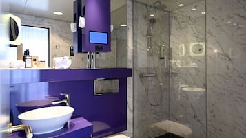 Ein modernes Badezimmer mit einem violetten Waschtisch, einem weißen Waschbecken, einer Toilette und einer Duschkabine.