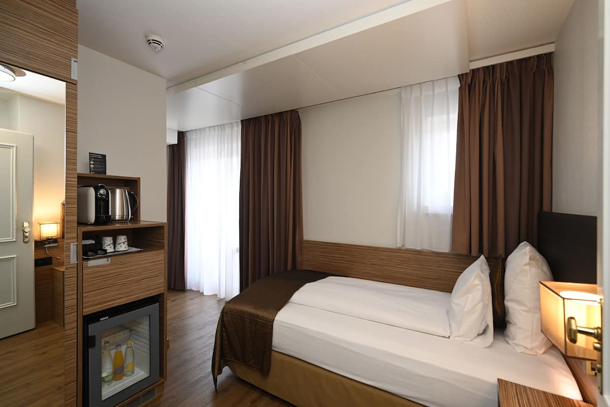 A hotel room with a bed, a minibar, a television, and a window with curtains.