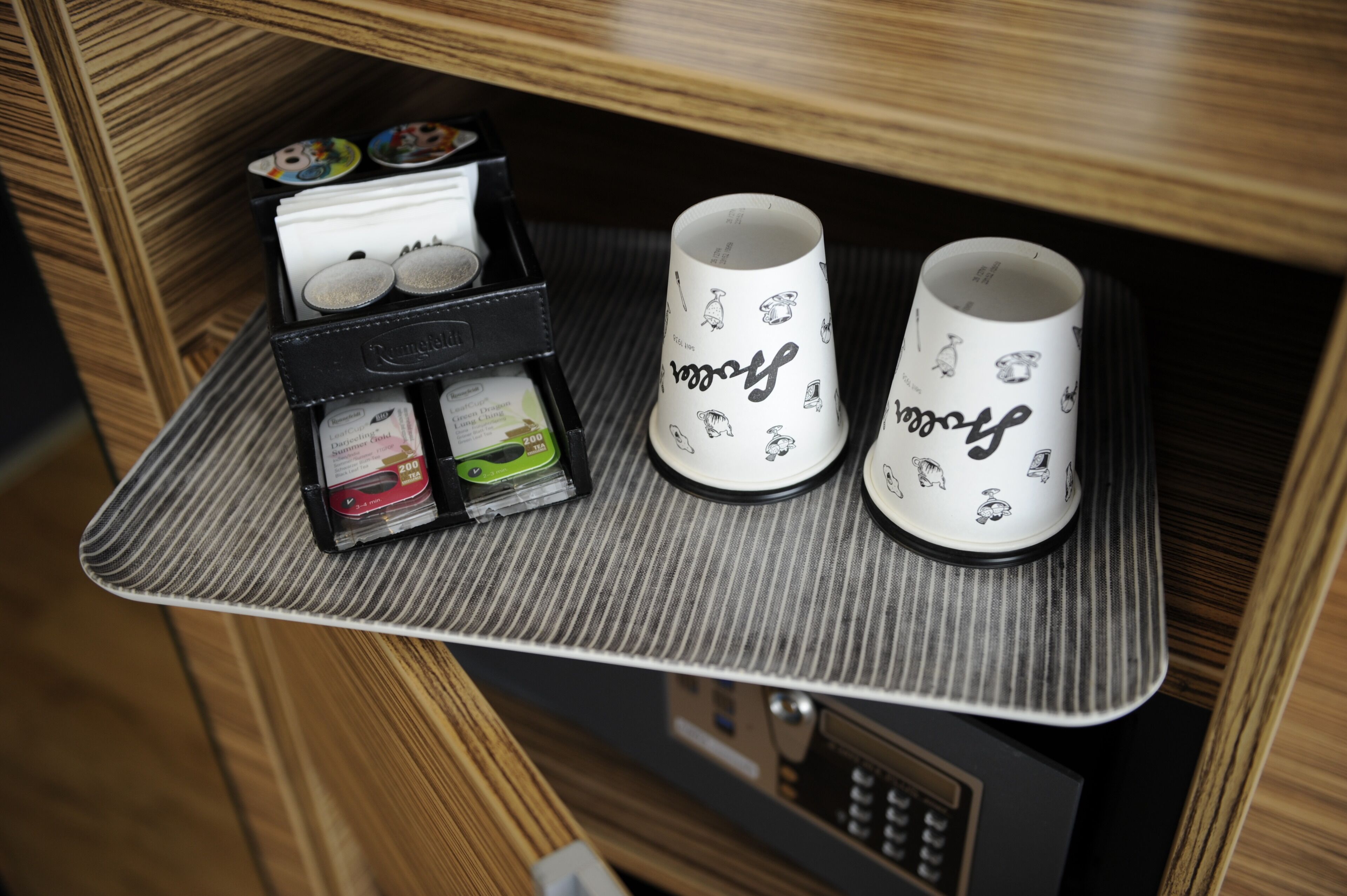 Una bandeja con dos tazas y una caja de bolsitas de té en un mueble de madera.