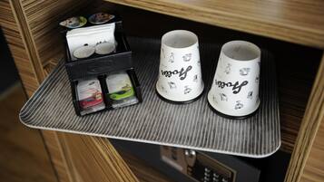Una bandeja con dos tazas y una caja de bolsitas de té en un mueble de madera.